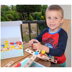 Child assembling Alexander Junior Wooden Airplane Set with colorful screws and connectors on a wooden table.