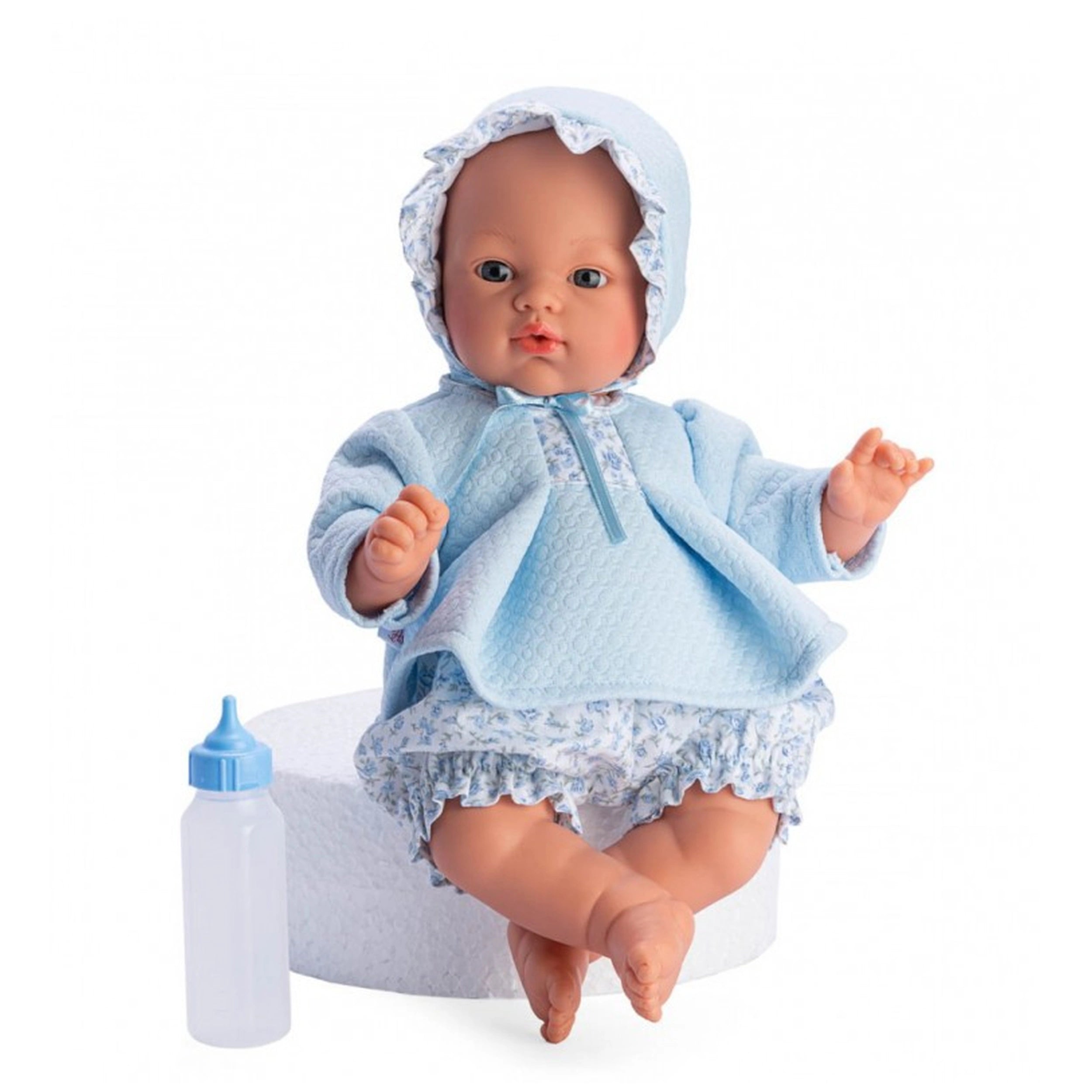 Soft-bodied doll with blue eyes and a bonnet, wearing a blue and flowered outfit, sitting next to a toy bottle.