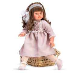 ASI Dolls Pepa in eggplant pique dress with flowered chest, seated on a woven basket.