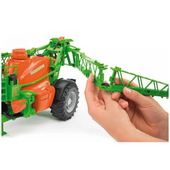 Hands adjusting the green arm of a Bruder Amazone UX 5200 toy field sprayer with orange tank.