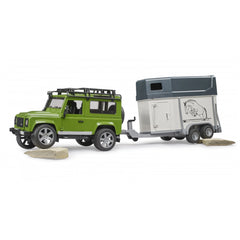 Green Land Rover Defender toy with detailed horse trailer on rocky terrain.