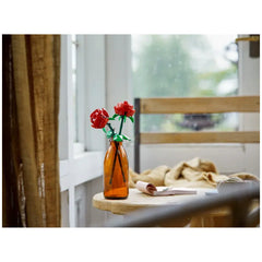 Red LEGO roses in an amber vase, set on a wooden table with a blurred background of a cozy room and natural light.