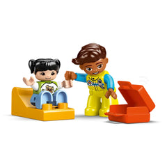 Two colorful DUPLO figures engage in a playful scene: one figure sits on a yellow slide, while the other, dressed as a paramedic, holds their hand. An open red toolbox sits nearby, adding to the imaginative rescue play theme.