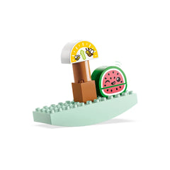 Colorful LEGO® DUPLO® watermelon toy on a green base, featuring a smiling face and a scale with animated bees above it, promoting playful learning.