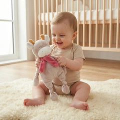 Artesavi Cow Plush Rattle 32 Cm held by smiling baby on a white rug in a cozy nursery setting.