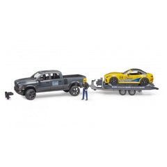 Bruder RAM Power Wagon toy with a yellow race car on a trailer, and a figure in a yellow helmet standing beside it.
