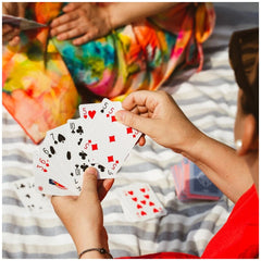 Dal Negro San Siro Pro Rummy Cards in blue-red deck held by hands against colorful fabric and a partially visible arm.