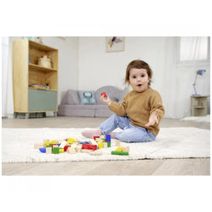 Eichhorn Baby Wooden Coloured Blocks are scattered around a child engaged in play on a white rug in a cozy indoor setting.