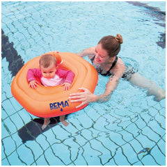 Happy People Bema Baby Swimming Seat in orange, surrounded by clear blue water with a woman and child enjoying the pool.