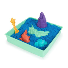 Kinetic Sand Sandbox Set features bright blue sand in a green container with sea creature toys and a purple castle on top.
