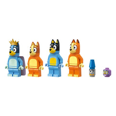 Four colorful LEGO minifigures from the Bluey series stand in a row: Bluey in blue with a crown, Bingo in orange, Bandit in black, and Chilli in orange. Additional accessories include a blue crayon and a purple block.