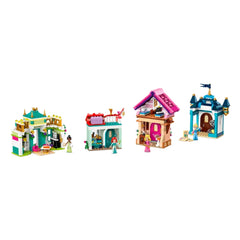 Four colorful LEGO® Disney Princess buildings are displayed. On the left, Tiana's restaurant features a dining area and a rooftop with storage. In the center, a building with a red roof includes unique decorations. The third building is pink and has playful details, while the rightmost structure is blue, showcasing elegant windows and a flag. Each building is surrounded by vibrant décor elements, ready for imaginative play.