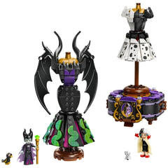 Two detailed dress models representing Maleficent and Cruella De Vil. Maleficent's dress features black wings and a green and purple skirt, while Cruella's dress is black and white with a polka dot pattern. Both dresses are displayed on elegant stands, accompanied by minifigures of the characters and their pets.
