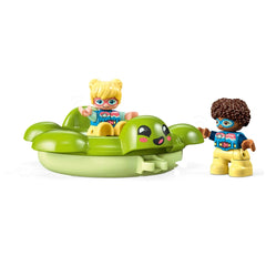 Two cheerful children playing with a green turtle float, one waving while sitting inside, the other standing beside, both wearing colorful shirts.