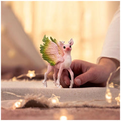 Magical fawn figurine with wings and a soft texture held by a hand in a warm indoor setting.