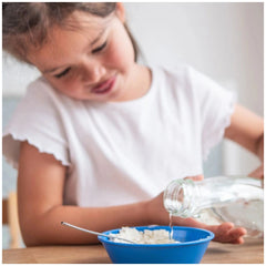 Teifoc sheepfold set features a young girl pouring liquid from a bottle into a blue bowl on a wooden dining table.
