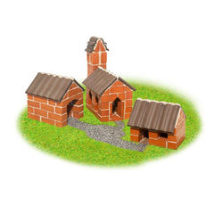 Teifoc Village set features two red brick buildings with thatched roofs on a green grassy area connected by a pebble pathway.