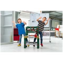 Theo Klein Bosch workbench with children playing, red table, green chair, smooth light floor, and white wall background.