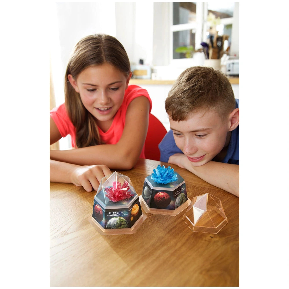 4M Crystal Growing Red Edition toy playset displayed on a wooden table with two children in red and blue shirts.