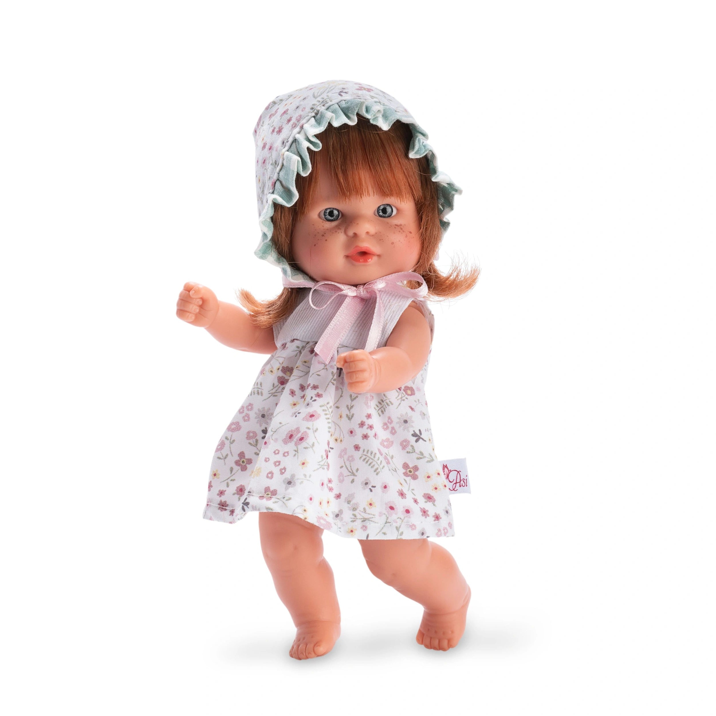 ASI Dolls Bomboncín Doll in floral dress with bonnet, standing with arms raised, showcasing red hair and a smiling expression.