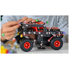 Child assembling Alexander Constructor Black Spider off-road toy with metal and red plastic pieces on table.