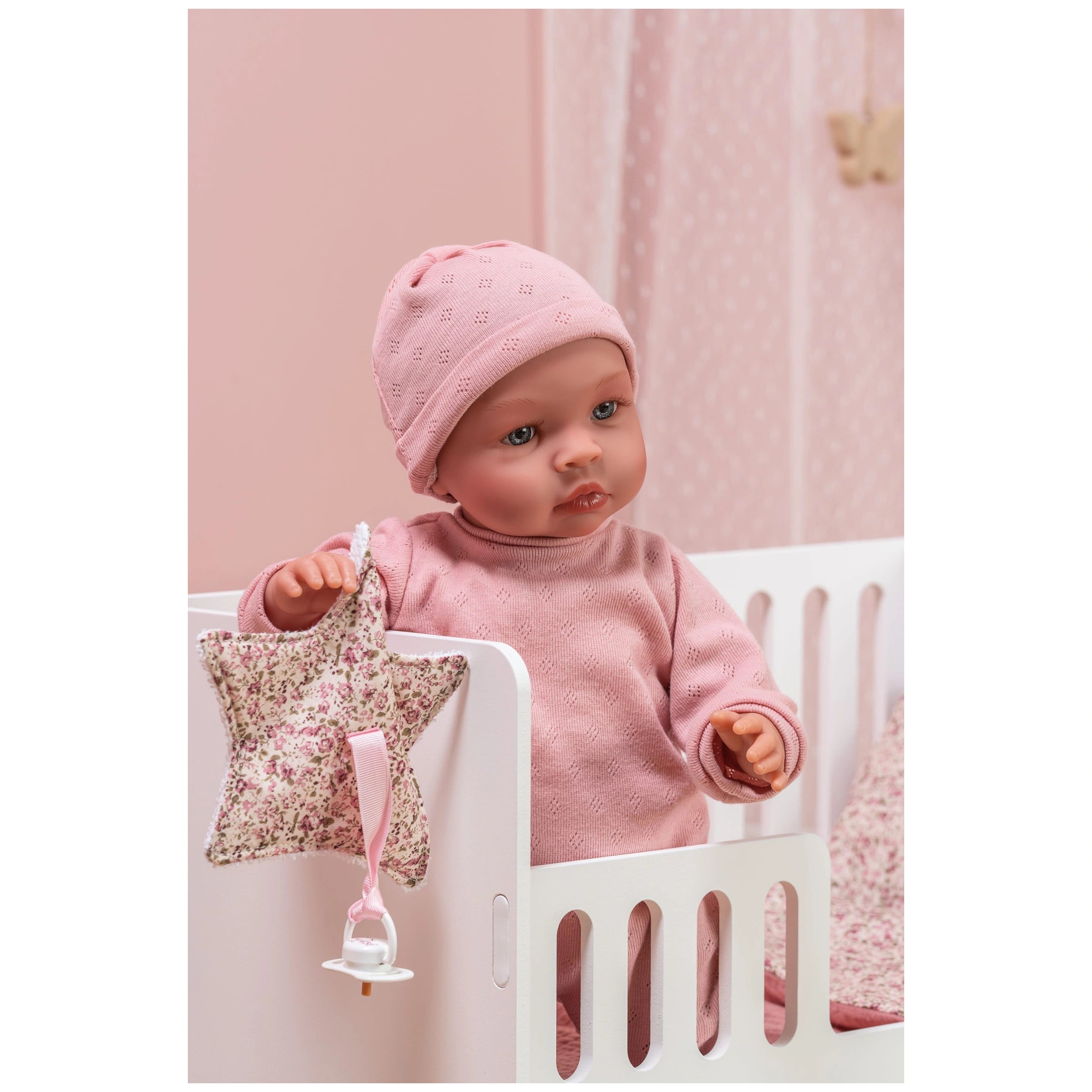 Doll in pink outfit in a crib with a star-shaped pacifier holder, from the Así Dreams Martina Collection.