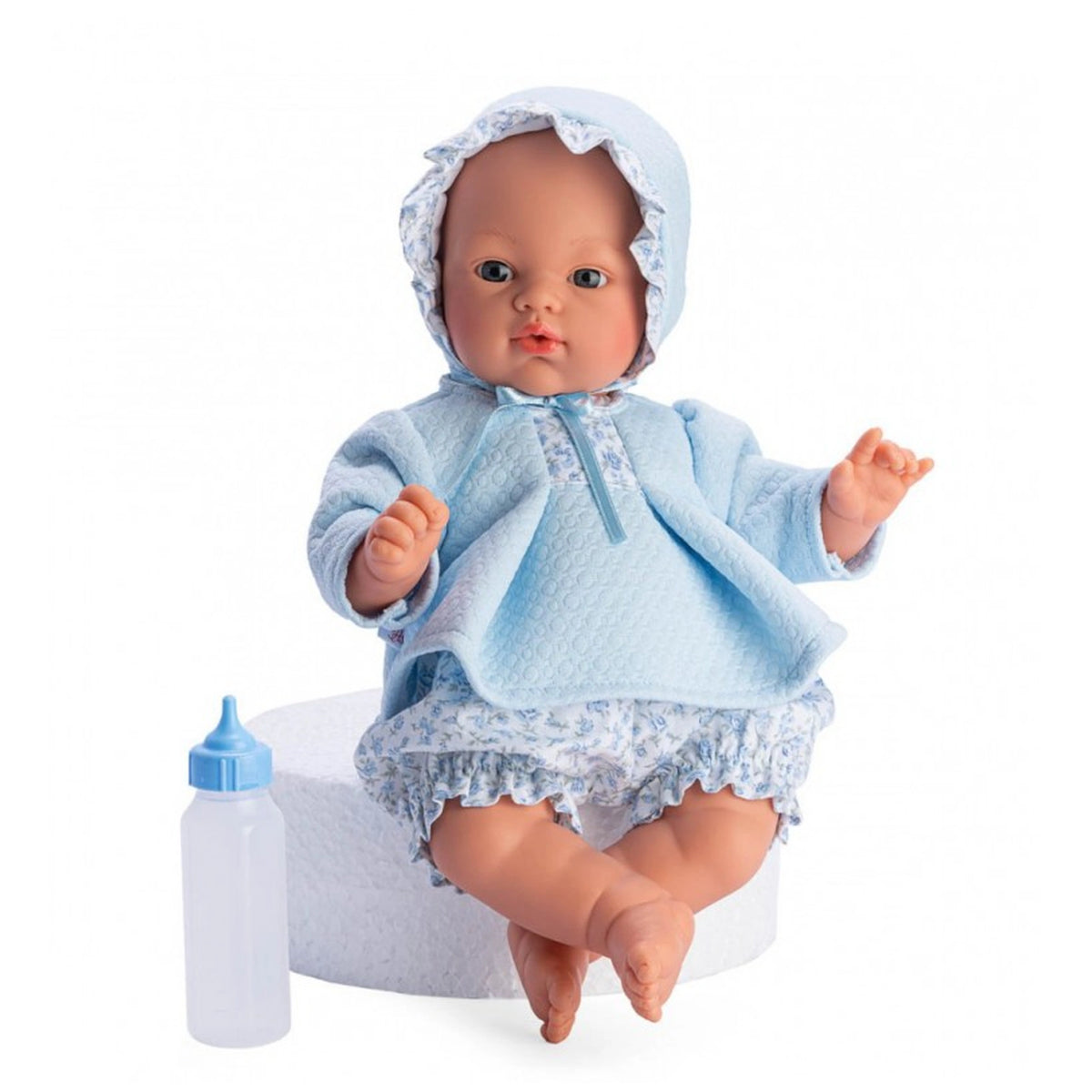 Soft-bodied doll with blue eyes and a bonnet, wearing a blue and flowered outfit, sitting next to a toy bottle.
