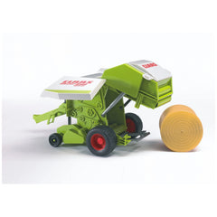 Green and white toy Claas Rollant 250 Straw Baler with red wheels, next to a rolled straw bale.