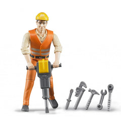 Bruder construction worker wearing an orange vest and yellow helmet holds a jackhammer, with various tools beside him.