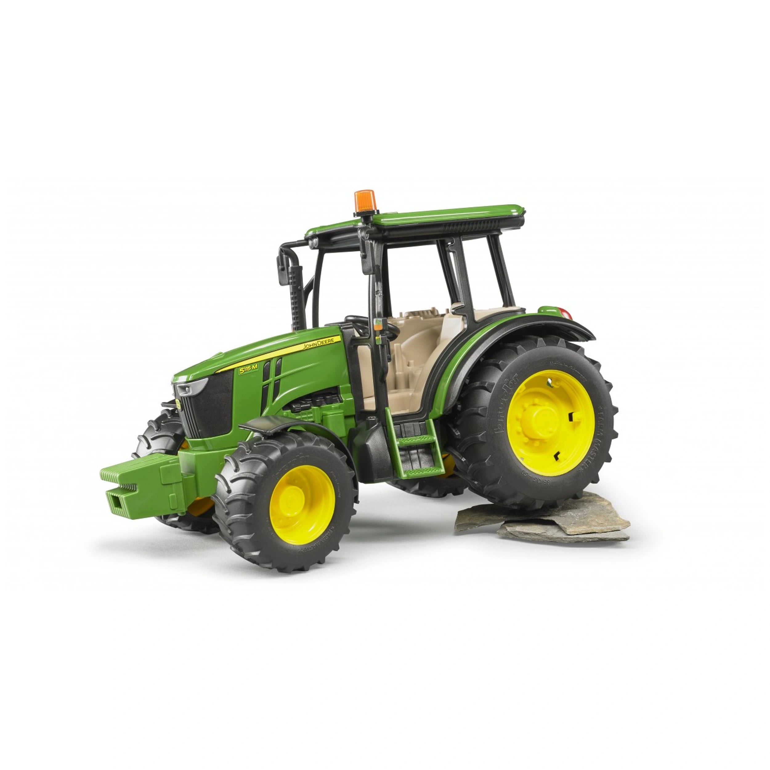Green Bruder John Deere 5115 M toy tractor with yellow wheels on rocky surface, showcasing its detailed design.