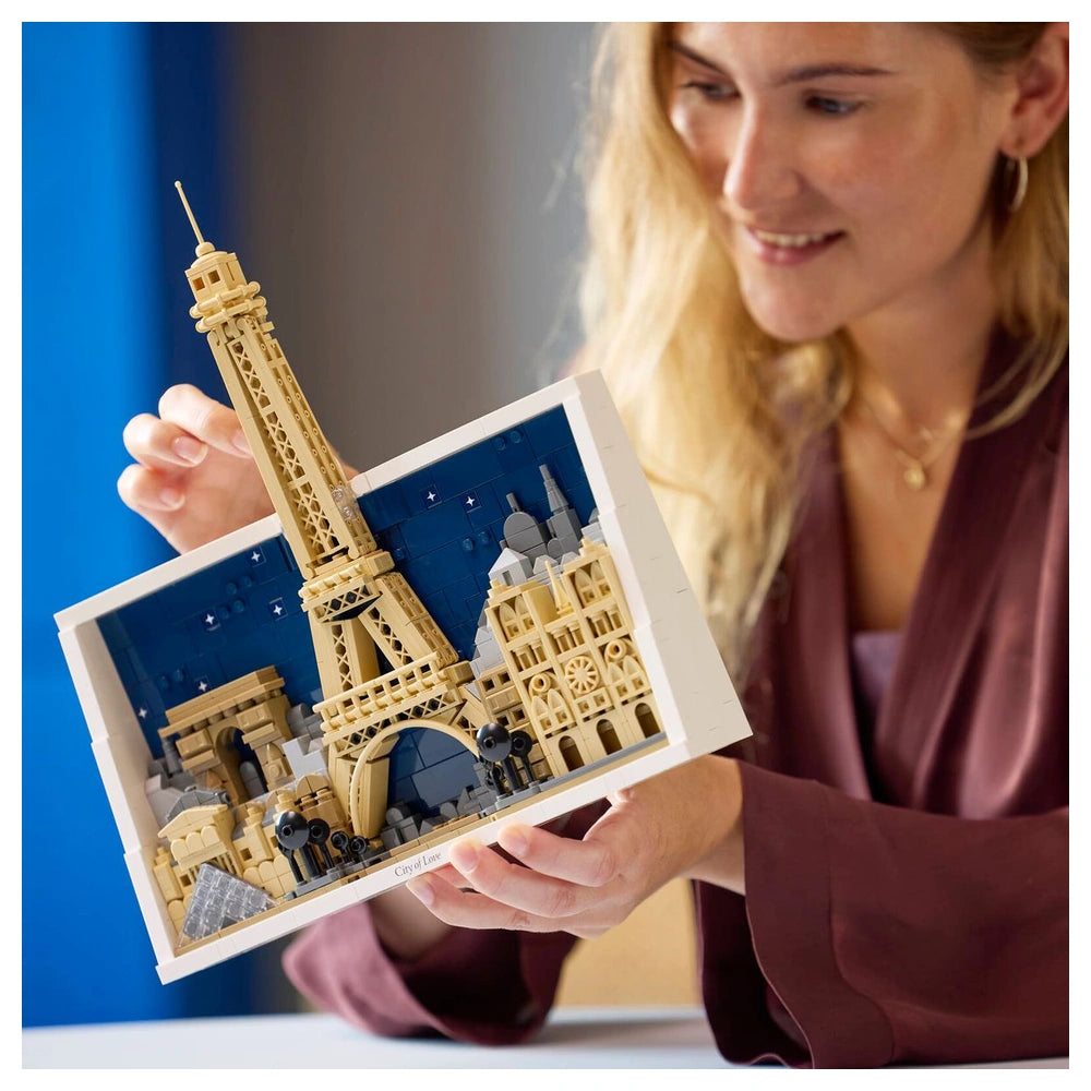 LEGO Eiffel Tower model held by a smiling woman in an indoor setting, showcasing detailed beige and brown plastic bricks.