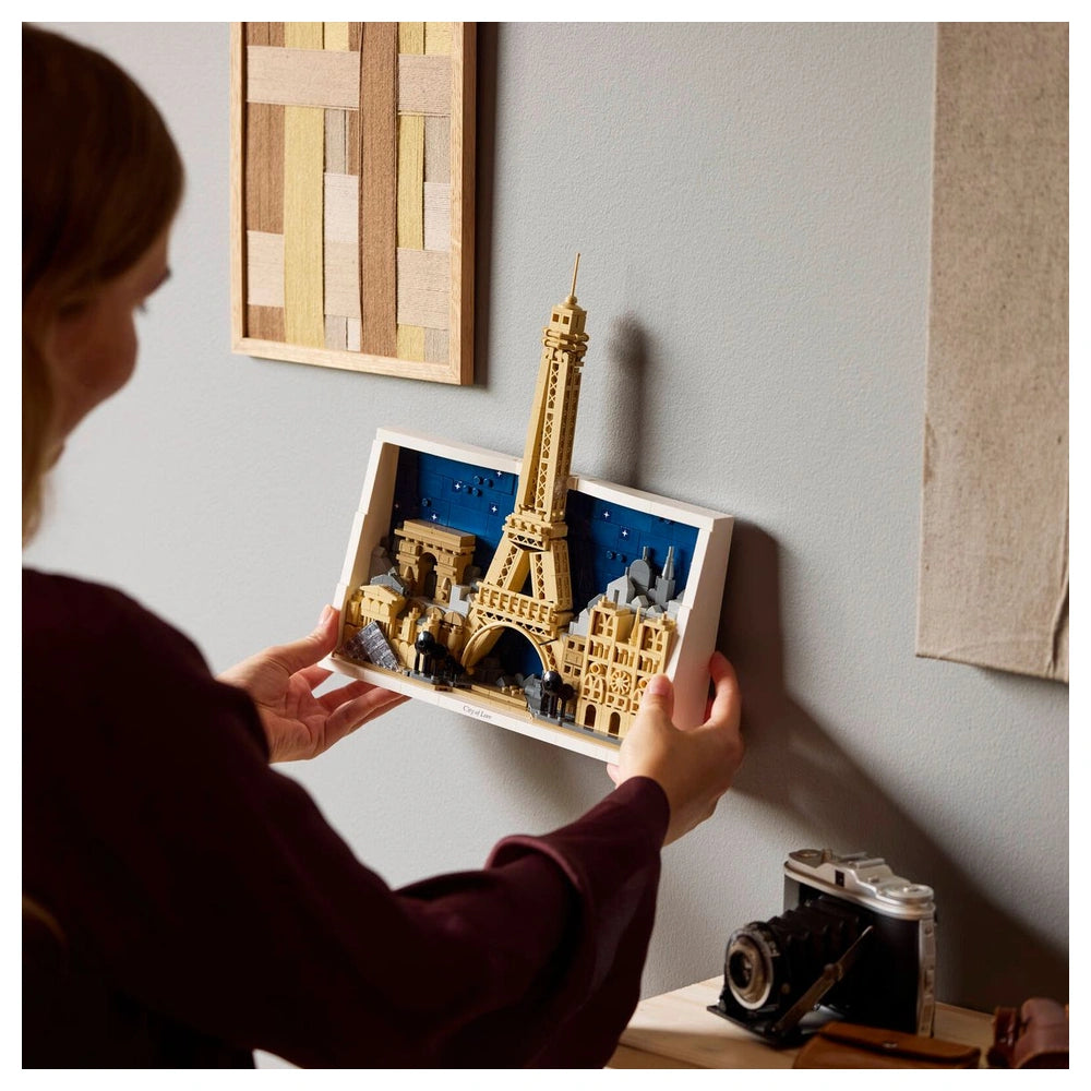 LEGO Architecture set featuring a person holding a detailed white Eiffel Tower model on a stand against a light grey wall.
