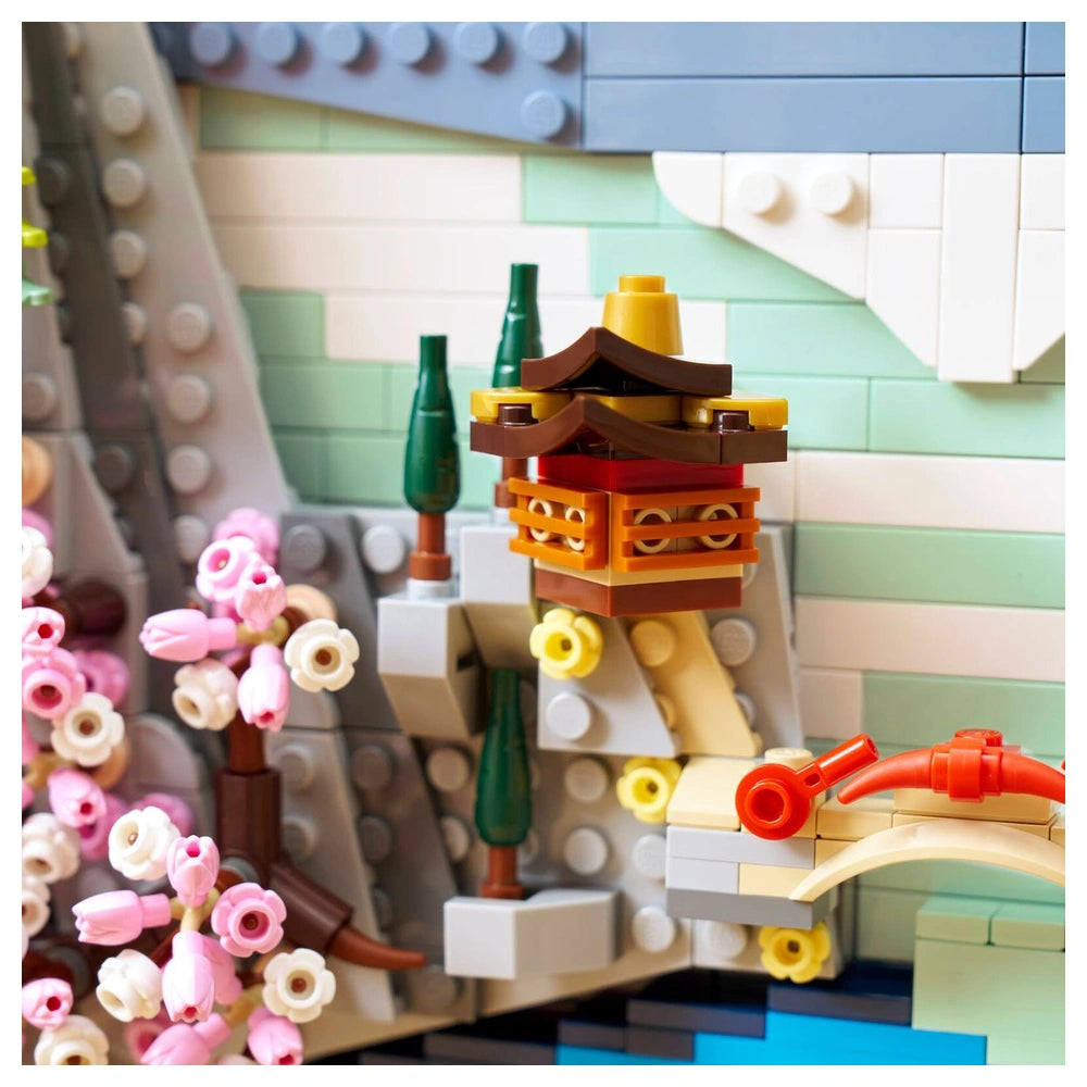 LEGO model of a Japanese cherry blossom landscape featuring a small building, flowers, and a green tree on a tiled floor.