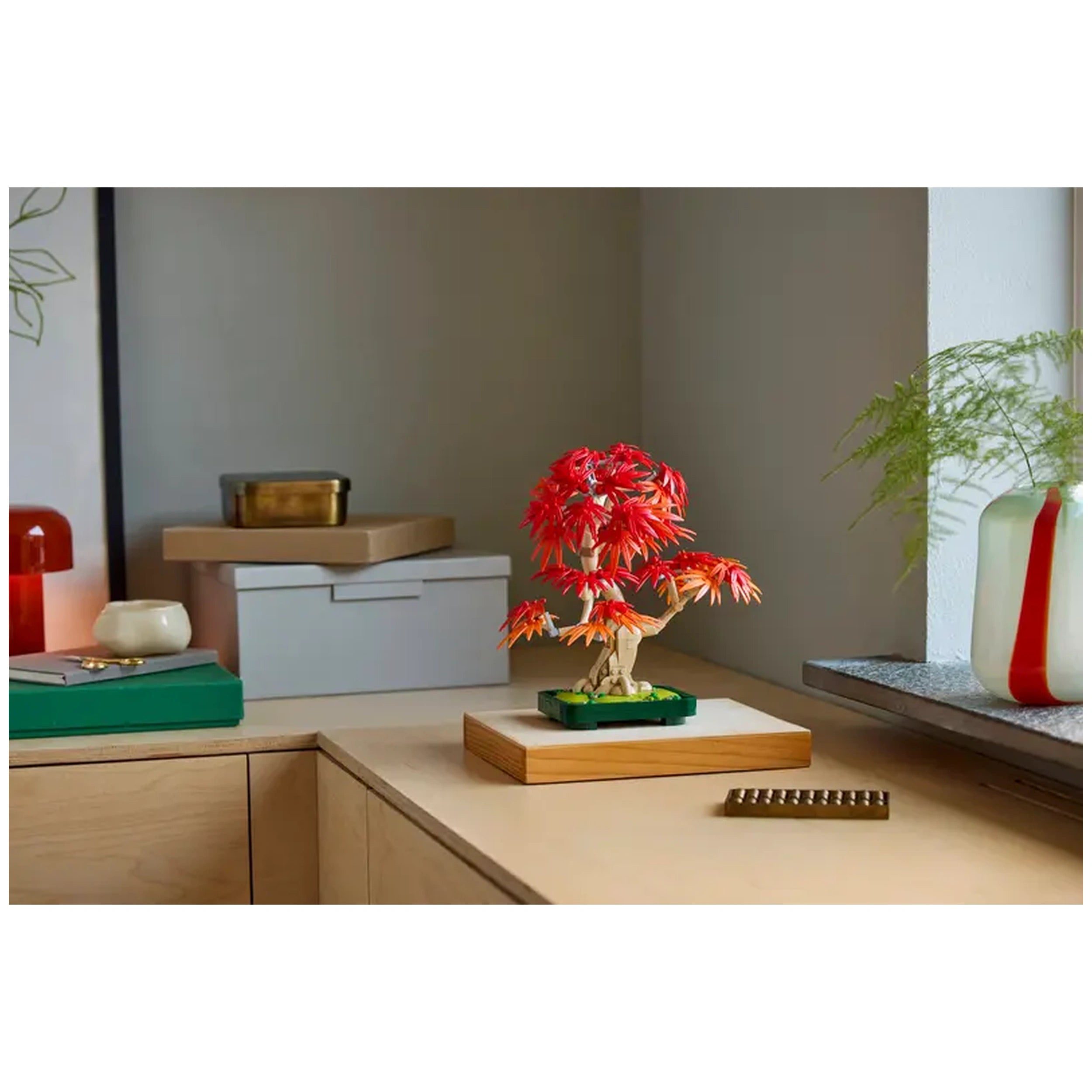 LEGO Botanicals Japanese Red Maple Bonsai Tree set displayed on a light wood surface, showcasing vibrant red and orange leaves in a dark green pot.