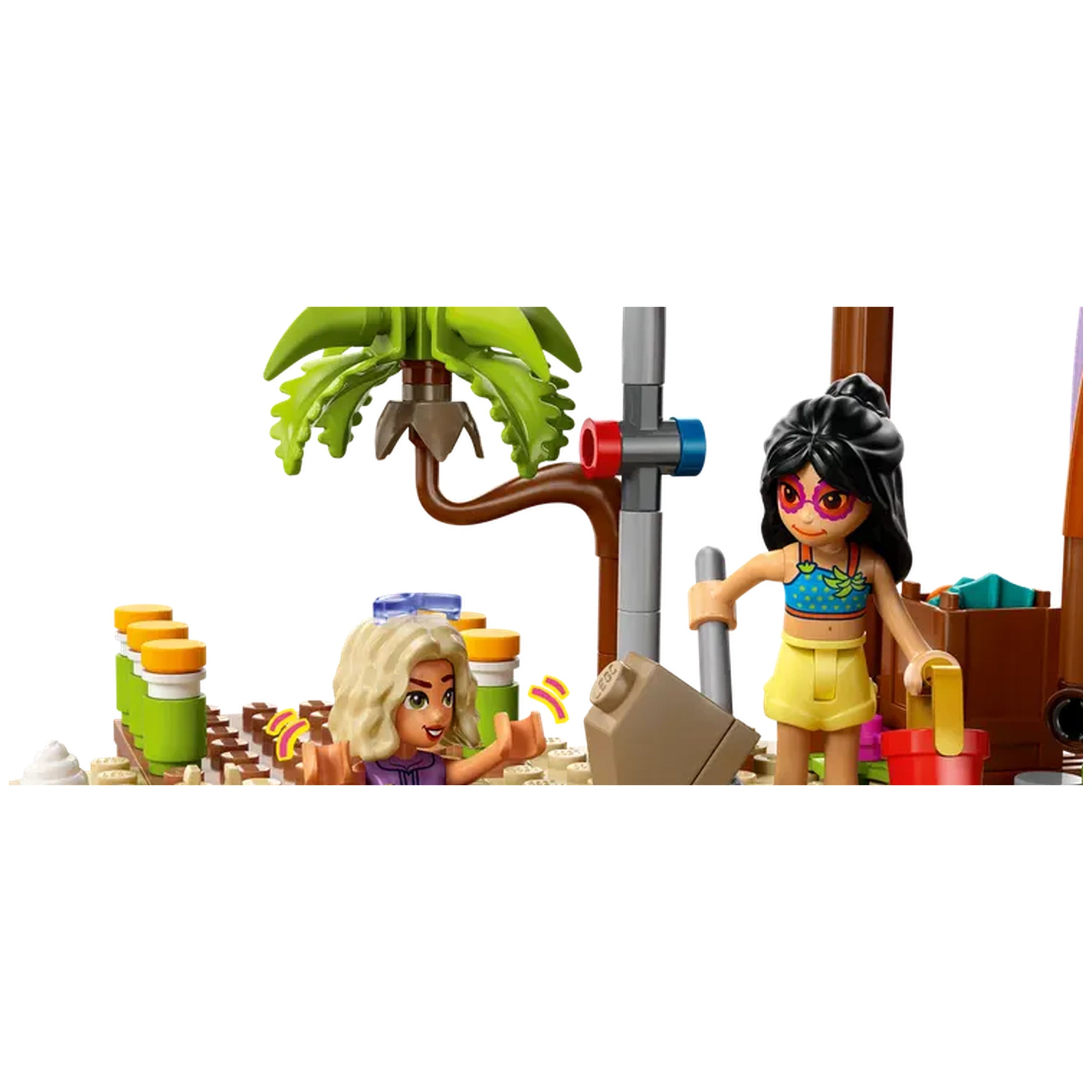 Two LEGO Friends minidolls enjoy a beach scene with a palm tree, sand, and colorful building accessories, engaging in playful activities.