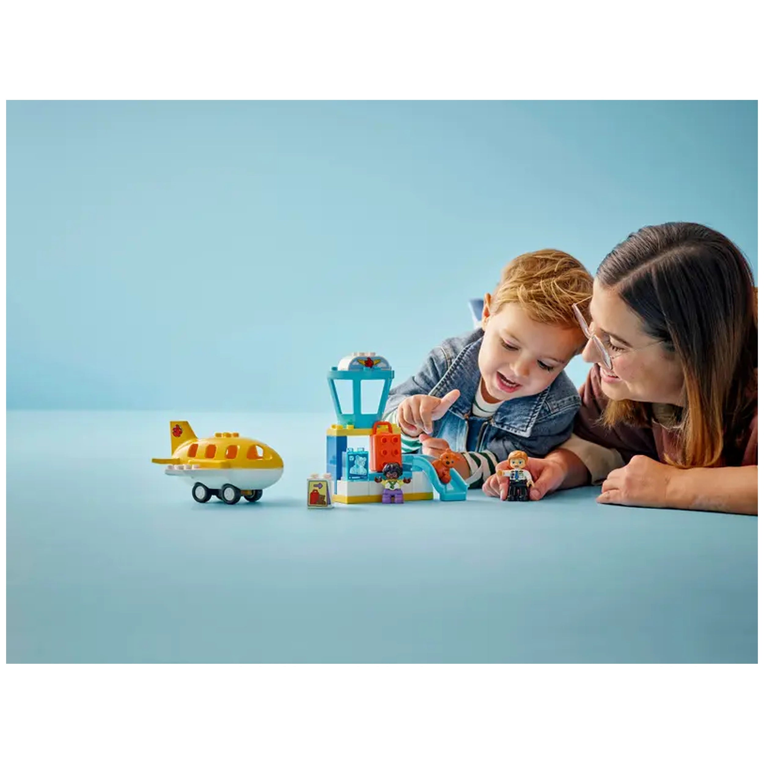 Child and adult play together with LEGO First Time at the Airport set, featuring an airport control tower and a yellow airplane on a blue background.