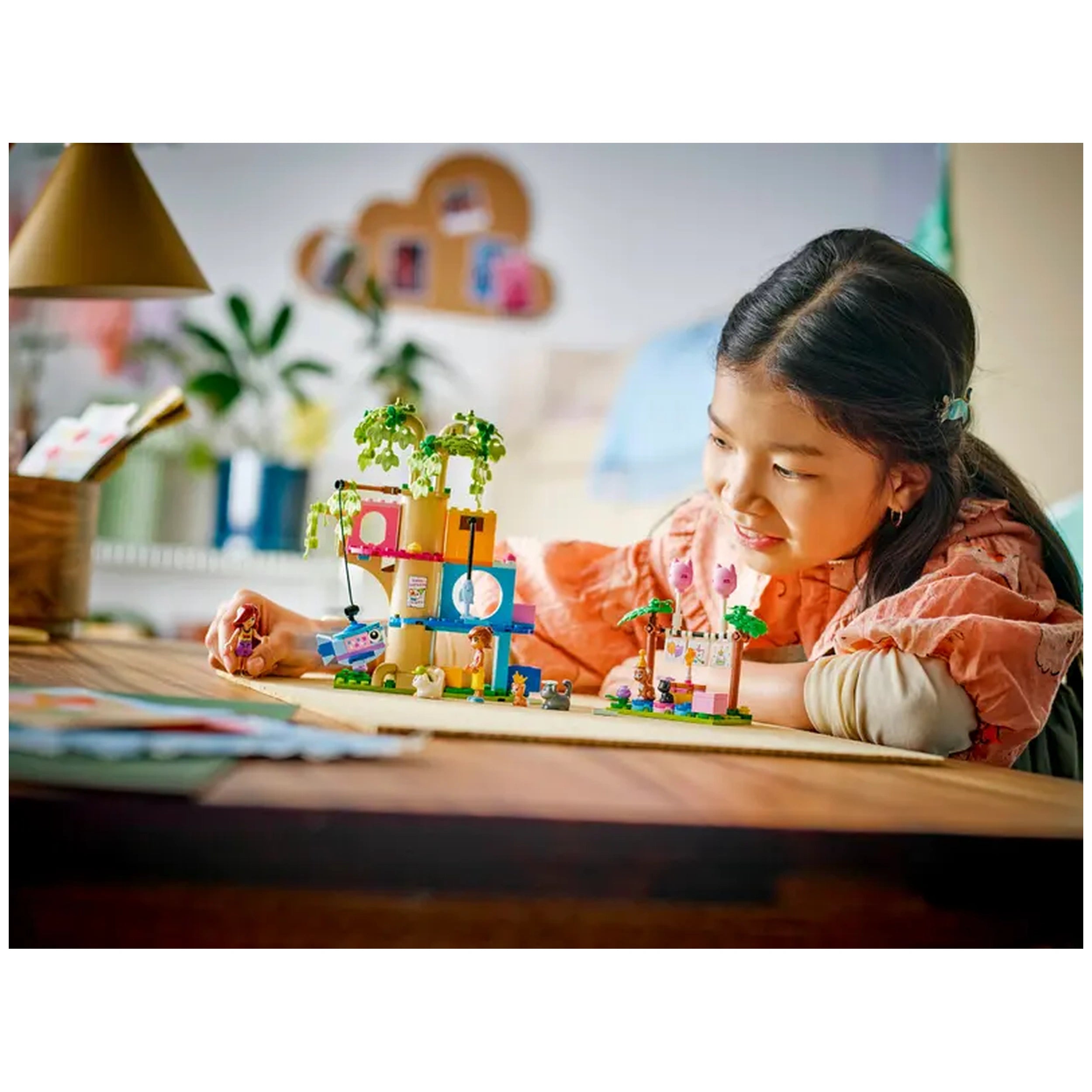 A young girl carefully plays with the LEGO Friends Cat Birthday Party & Tree House set, smiling as she arranges colorful building blocks and accessories. The bright, vibrant scene features two minidolls, playful cat figures, and festive decorations, creating a joyful atmosphere for imaginative play. A soft, warm light enhances the cozy indoor setting.