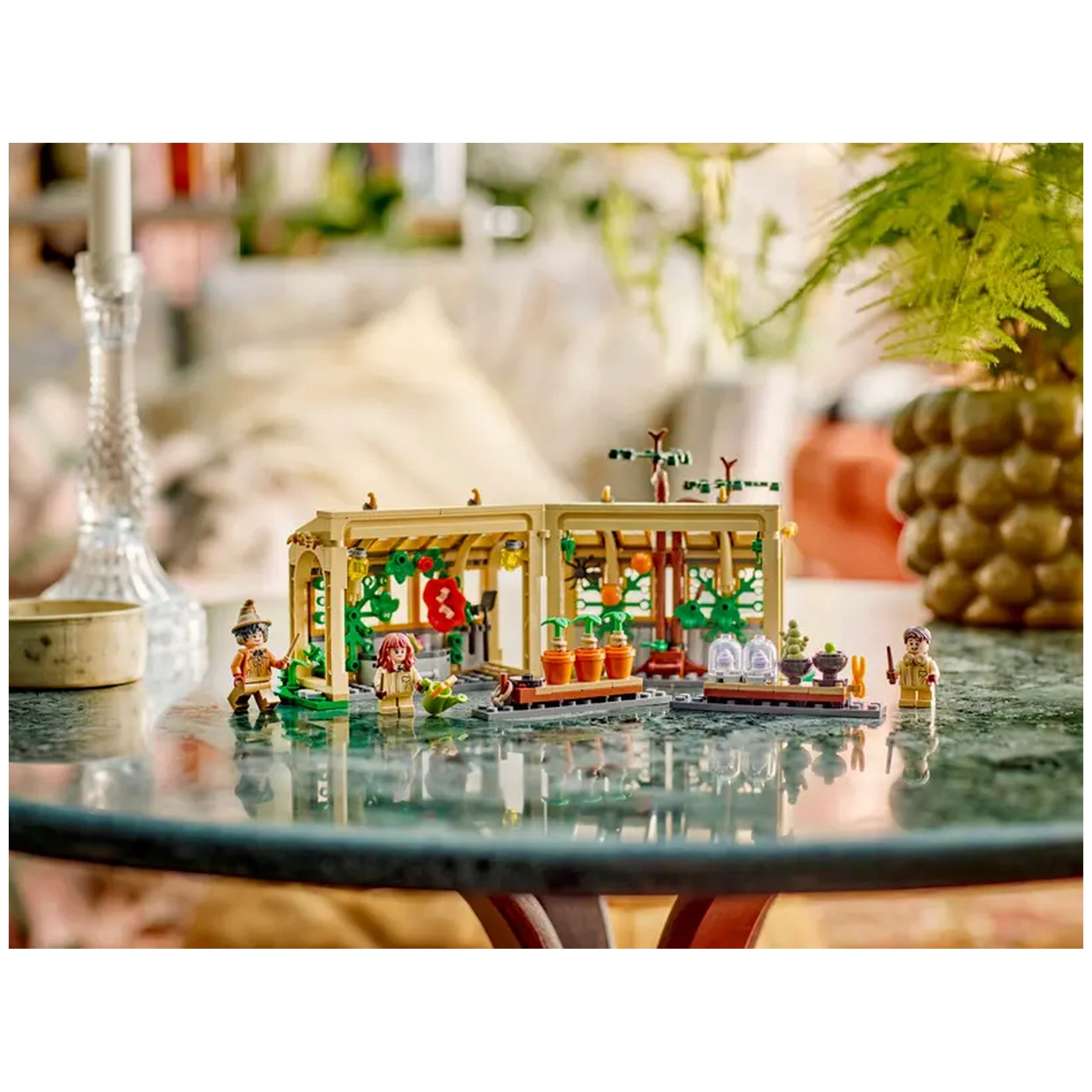 LEGO Hogwarts™ Castle Herbology Class set on a green table, featuring a greenhouse, potted plants, and three minifigures.