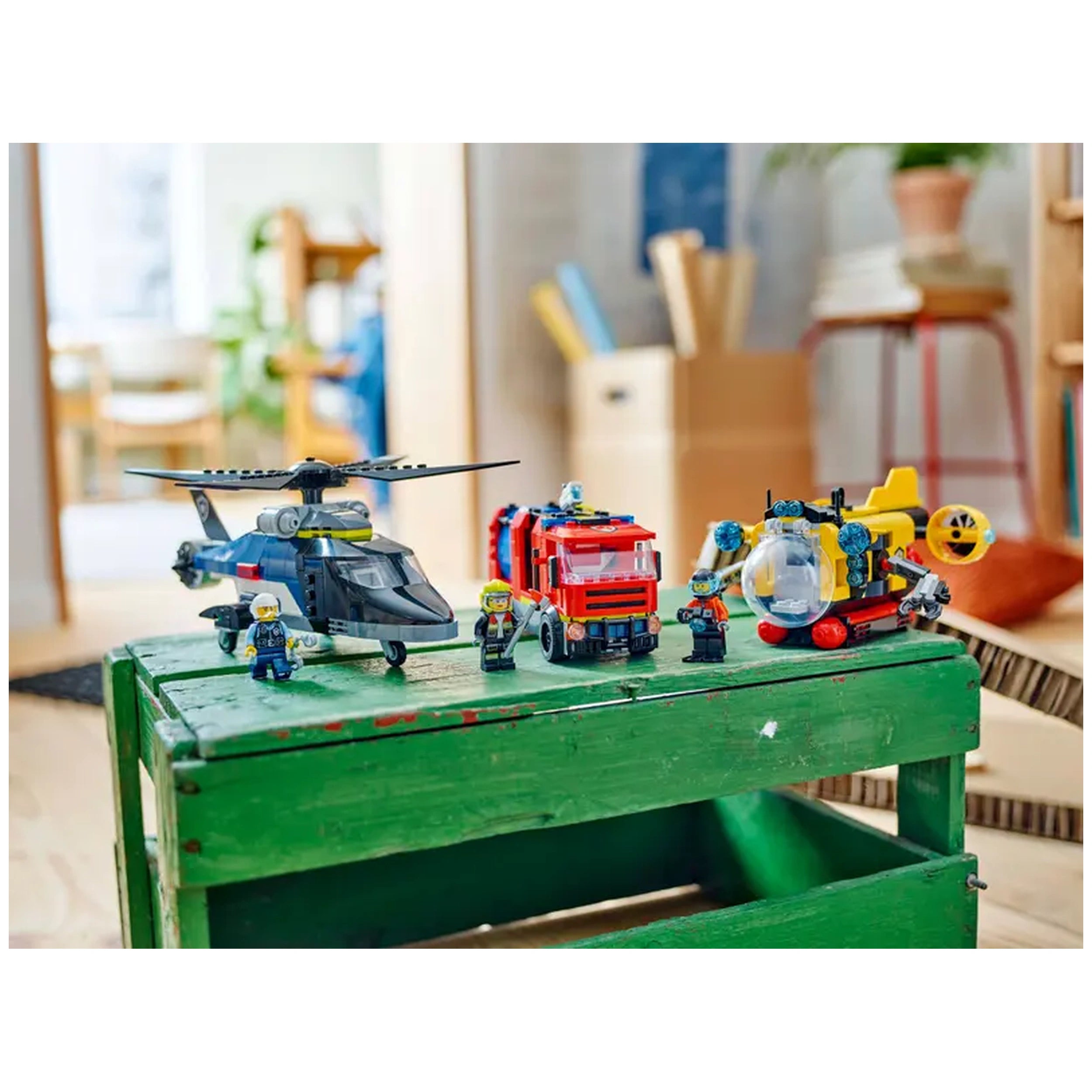 LEGO® City set featuring a police helicopter, fire truck, and exploration submarine on a green wooden crate, surrounded by LEGO® mini-figures.