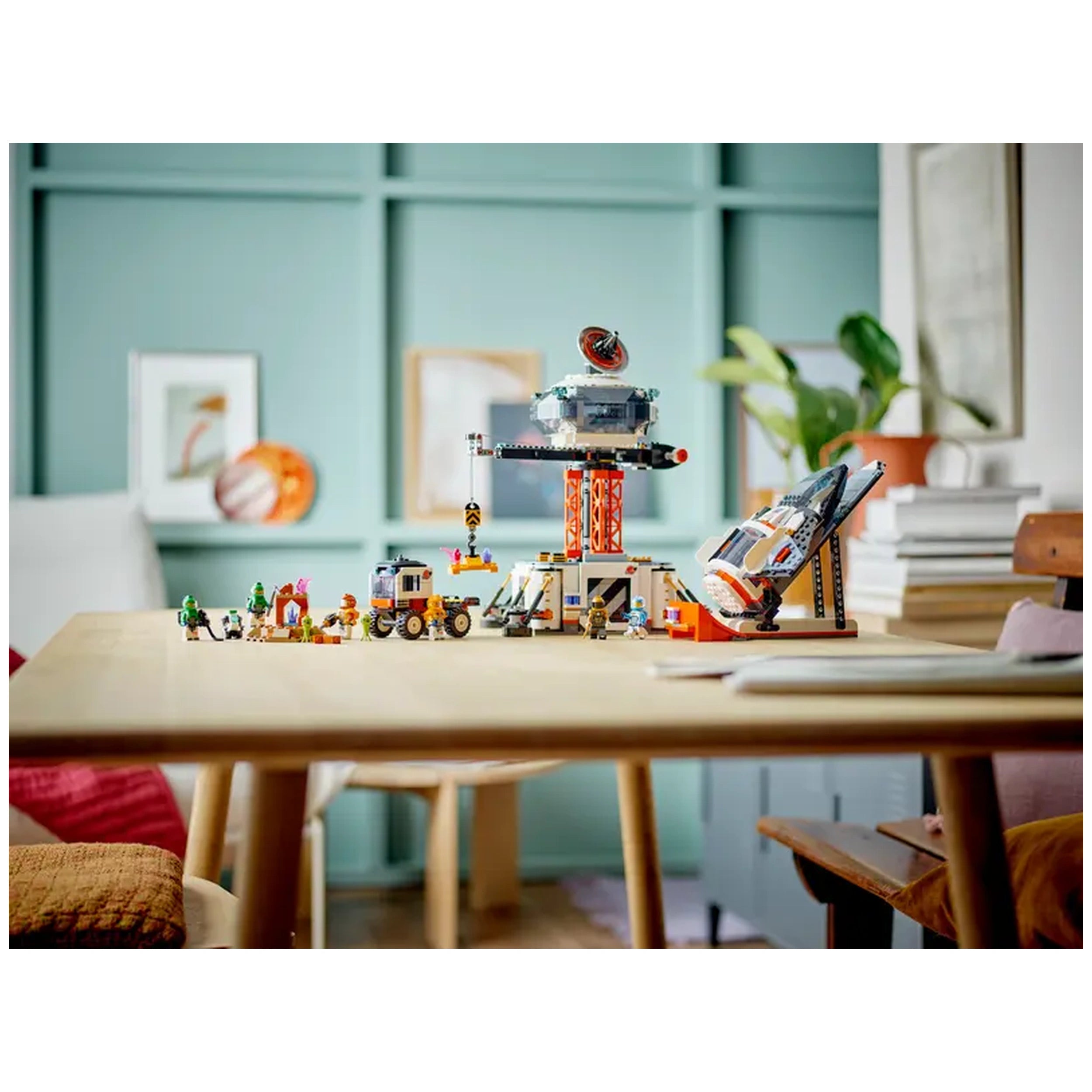LEGO City Space Base and Rocket Launchpad set displayed on a wooden table, featuring a colorful space station, vehicles, and astronaut minifigures against a light green background.