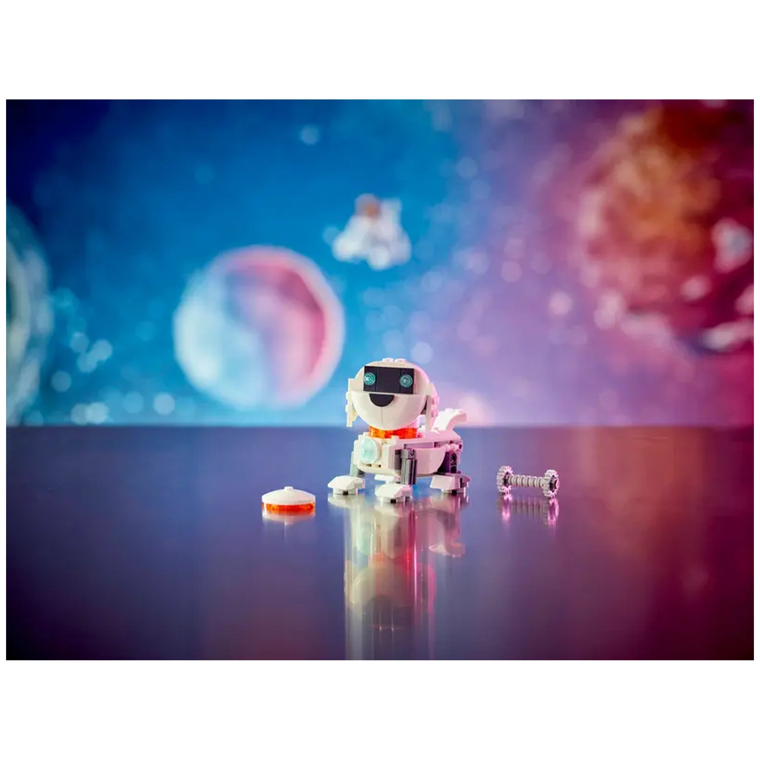 A colorful LEGO® Creator 3in1 Space Robot sits on a reflective table, smiling with blue eyes and a white body. Behind it, a vibrant outer space backdrop features planets and a distant astronaut. Nearby, a small space dog figure and a round piece lie on the table, ready for imaginative play.