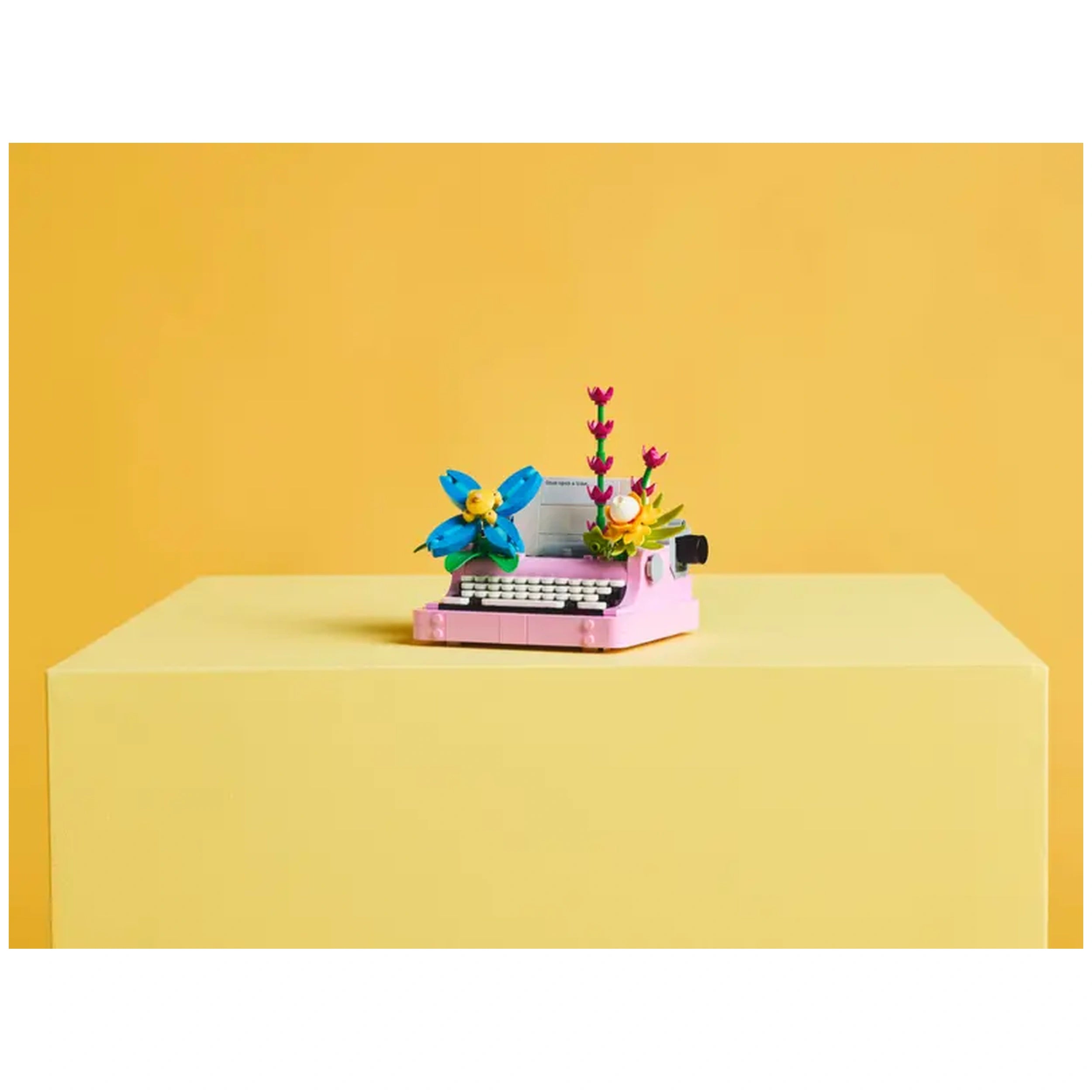 LEGO Creator Typewriter in pink adorned with blue and yellow flowers, set on a light yellow table against a vibrant yellow background.