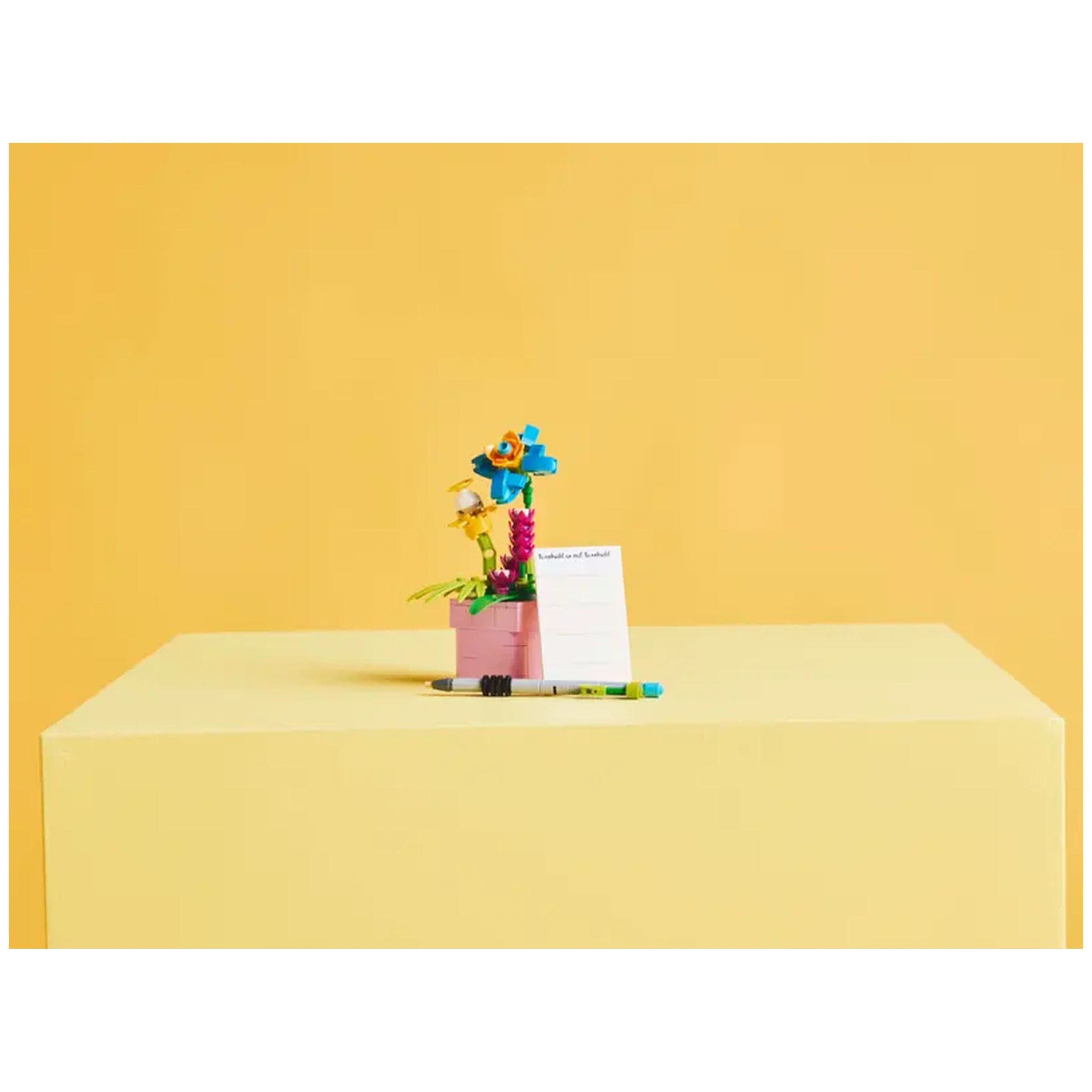 Colorful LEGO Creator Typewriter construction set featuring a mini typewriter, vibrant flowers, and a notepad on a pastel yellow background.