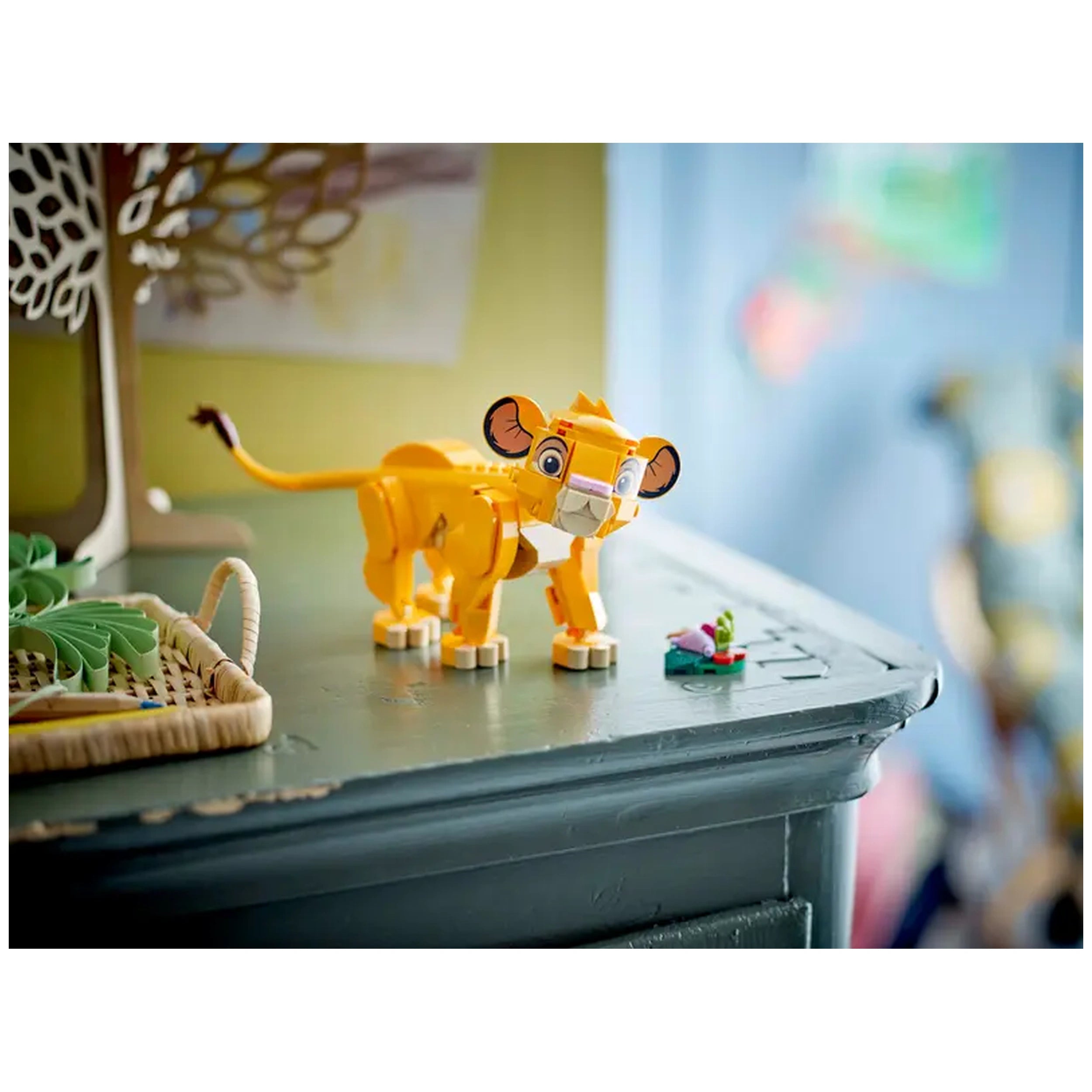 LEGO® Disney Simba the Lion King Cub construction set on a wooden table, featuring a vibrant yellow Simba figure with movable parts and a small leaf build with four colorful 'bugs' beside it.