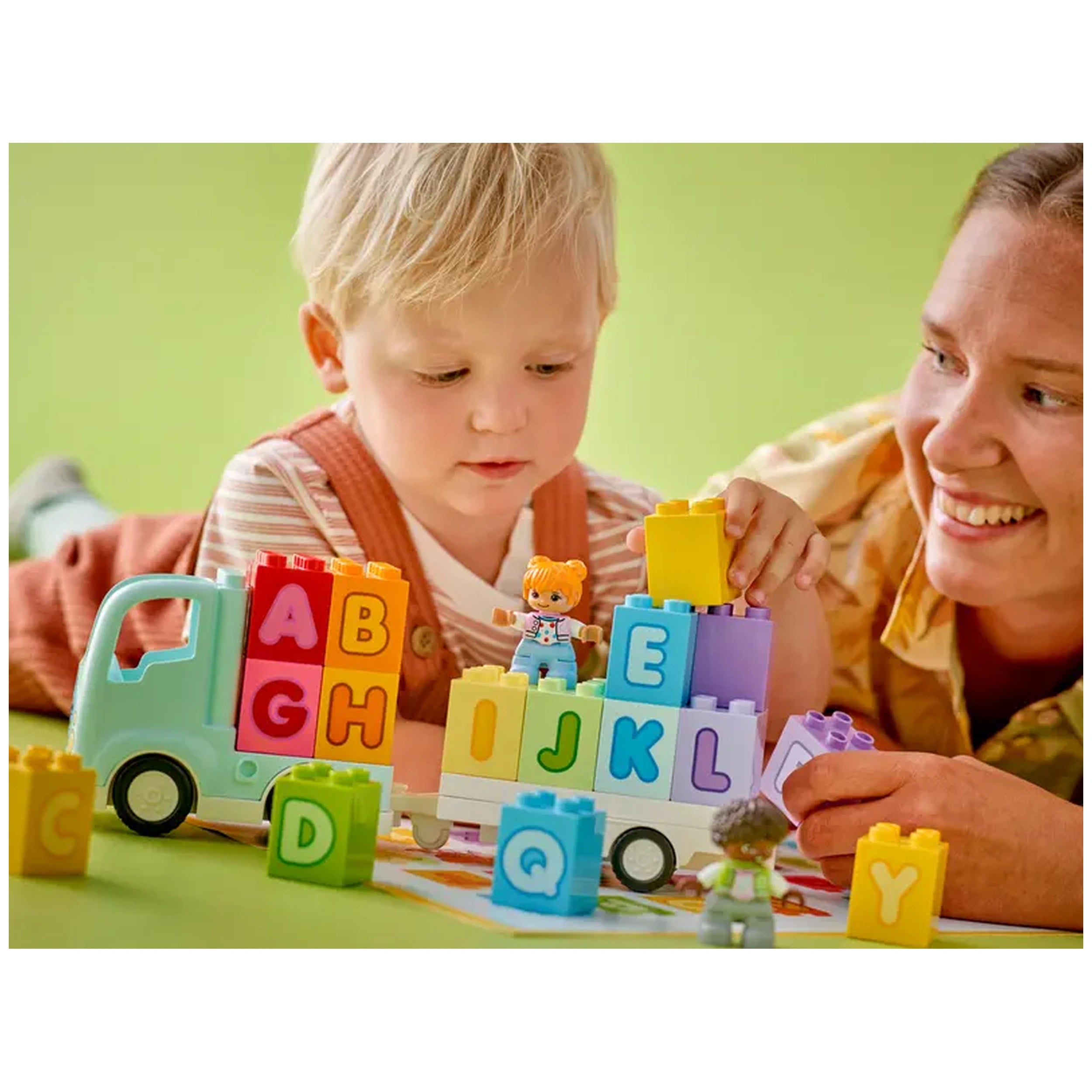 A young child and an adult play together with colorful LEGO® DUPLO® blocks, building a truck with letters A to L, on a green background.
