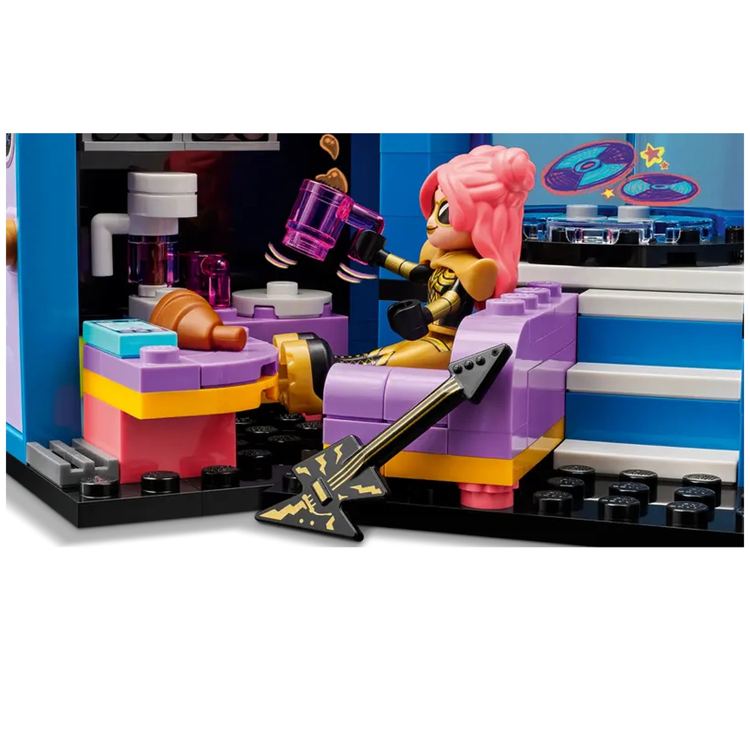 A mini-doll with pink hair sits on a purple chair, holding a pink drink. Beside her is a black guitar, and the colorful set includes a toy stage and music-themed decorations.