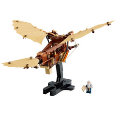 LEGO® Icons Leonardo da Vinci's Flying Machine model with tan flappable wings, mounted on a black stand, alongside a minifigure of da Vinci holding a design sketch.