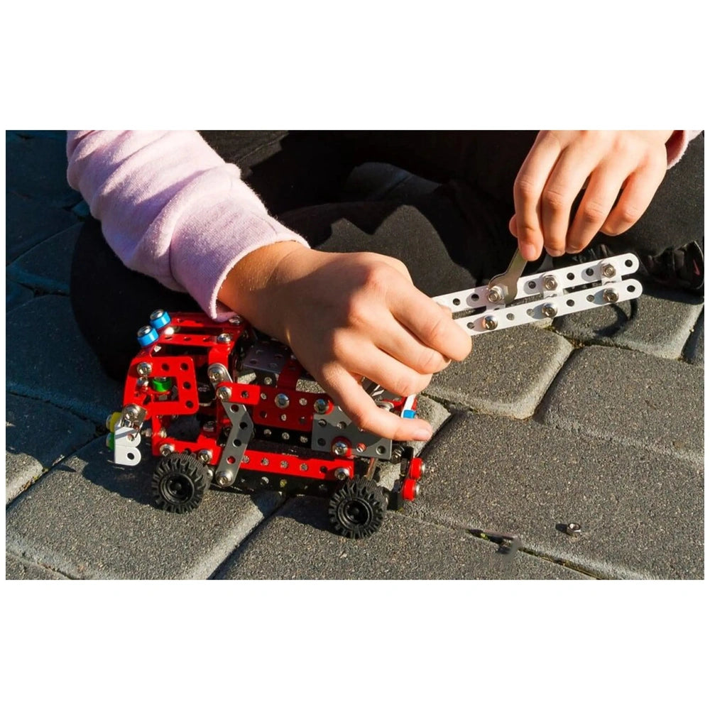 Child assembling Alexander Maly Constructor Fire Department set, red and silver pieces, on a paved surface.