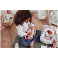 Child nurturing ASI María doll in Cloe dress, bottle-feeding on a cozy rug with dolls and accessories nearby.