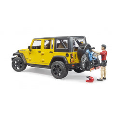 Yellow Jeep Wrangler Rubicon toy with mountain bike on rear rack, cyclist figure in red shirt beside, helmet on ground.